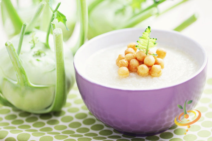 Creamy kohlrabi soup garnished with chickpeas in a purple bowl with fresh kohlrabi bulbs in the background