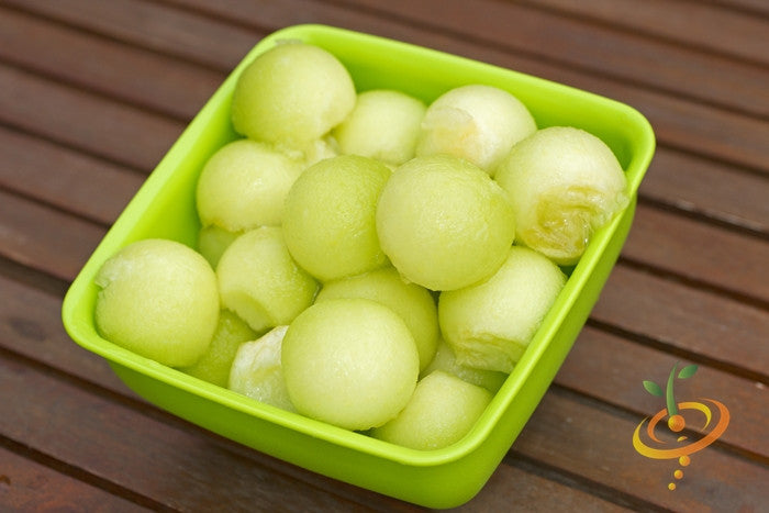 Green flesh honeydew melon balls in a green bowl on a wooden surface