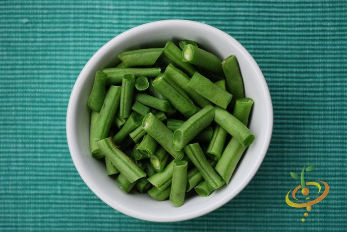 Chopped Tendergreen Bush Bean pieces in a white bowl on a green textured surface