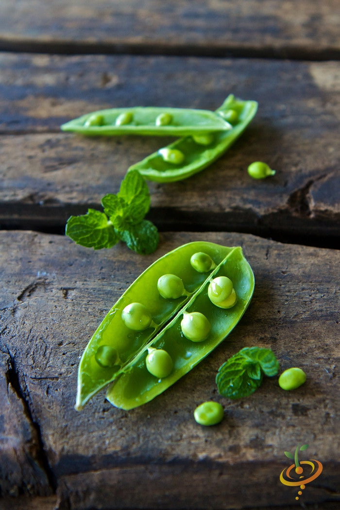 Close-up of fresh green sugar snap peas in open pods on rustic wooden surface with mint leaves