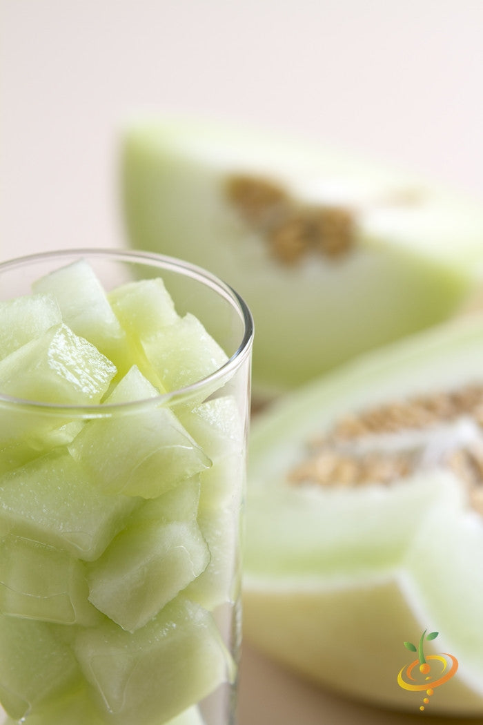 Glass filled with diced honeydew melon pieces and honeydew melon slices in the background
