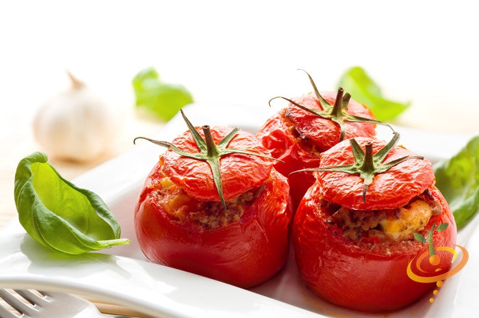 Three stuffed Caribe tomatoes on a white plate with basil leaves and garlic in the background