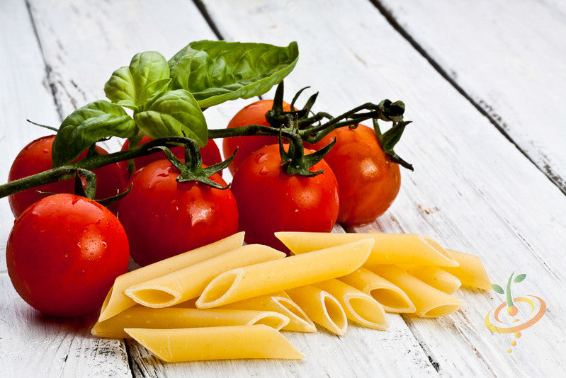 Italian Large Leaf Basil leaves on vine with fresh tomatoes and uncooked penne pasta on white wooden surface